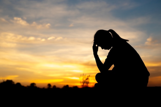 Silhueta de mulheres tristes e deprimidas sentadas na passarela do parque com o pôr do sol