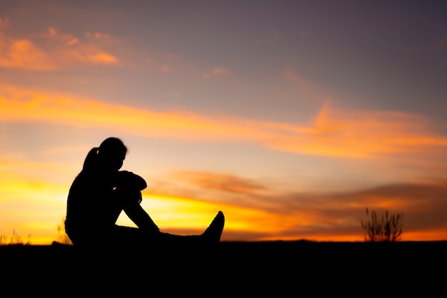 Silhueta de mulheres tristes e deprimidas sentadas na passarela do parque com o pôr do sol