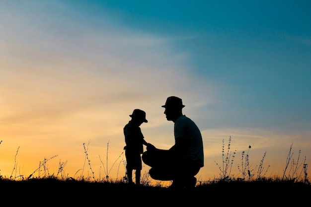 Silhueta de pai e filho felizes brincando no pôr do sol