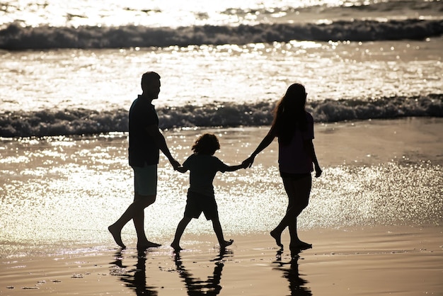 Silhueta de pai mãe e filho filho de mãos dadas e andando na praia