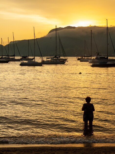 Foto silhueta de pescador na frente de barcos ao pôr do sol no brasil. cena da hora de ouro.