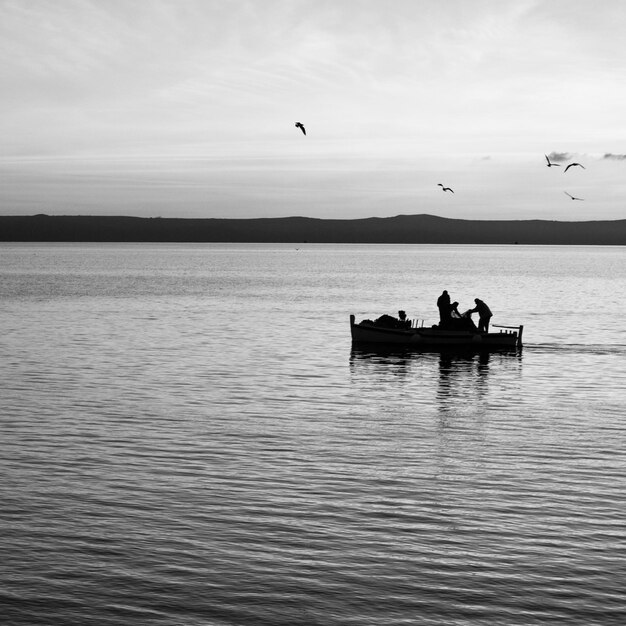 Foto silhueta de pescadores trabalhando em um barco no mar contra o céu laranja