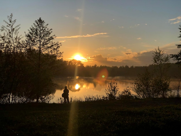 Silhueta de pessoa admirando o pôr do sol na paisagem de verão da margem do lago