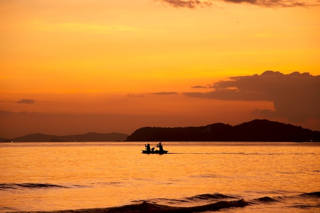 Silhueta de pessoas a remo de barco no mar ao pôr do sol
