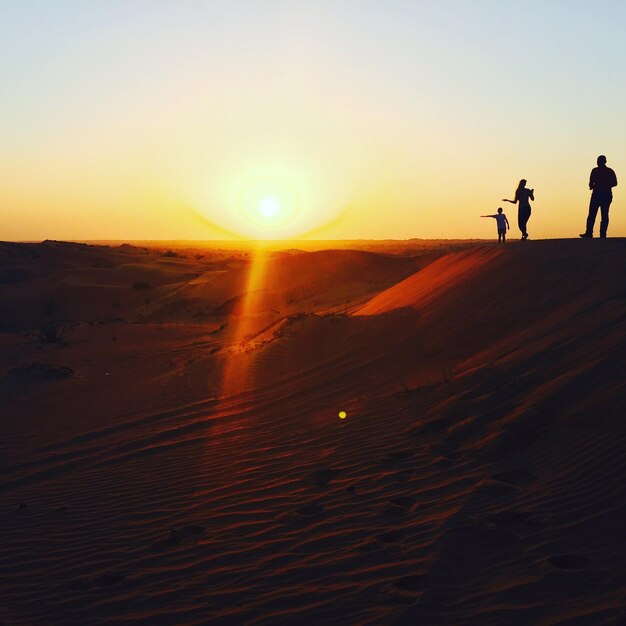 Foto silhueta de pessoas caminhando no deserto contra o céu claro durante o pôr do sol