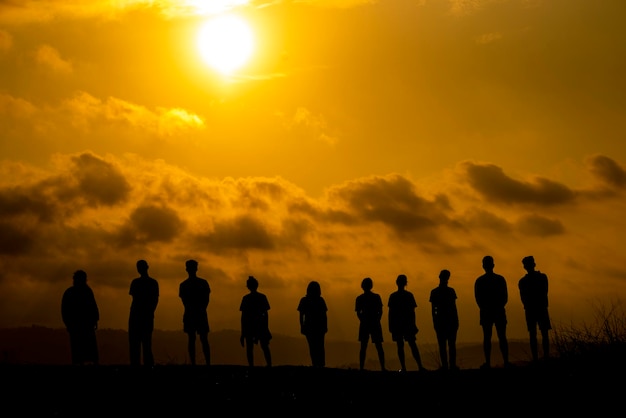 Silhueta de pessoas de pé em terra contra o céu nublado durante o pôr do sol