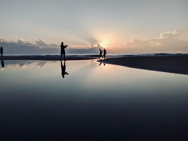 Silhueta de pessoas de pé junto ao mar contra o céu durante o pôr-do-sol