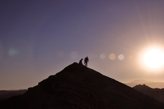 Silhueta de pessoas de pé no pico da montanha