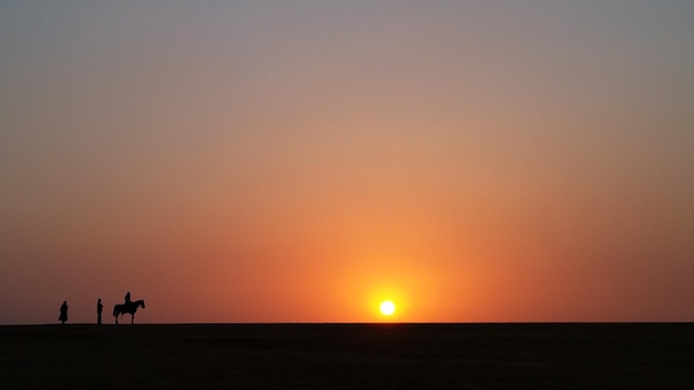 Silhueta de pessoas e cavalos em uma paisagem vazia durante o pôr do sol
