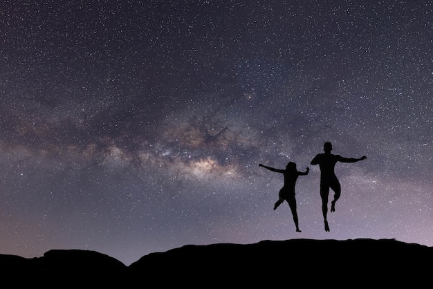 Foto silhueta de pessoas felizes pulando sobre o céu noturno com estrelas e galáxia via láctea astronomia oriente