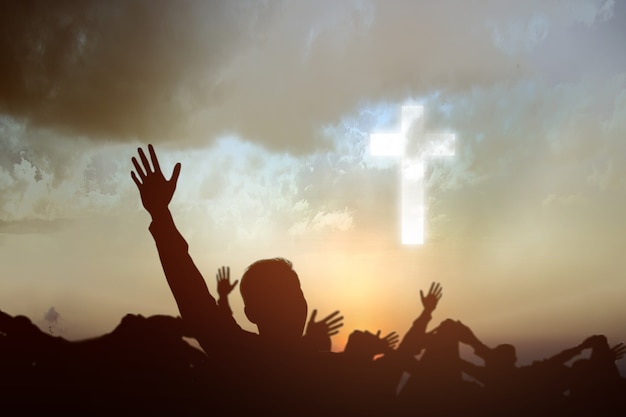 Silhueta de pessoas olhando para a cruz cristã com um fundo do céu ao pôr do sol