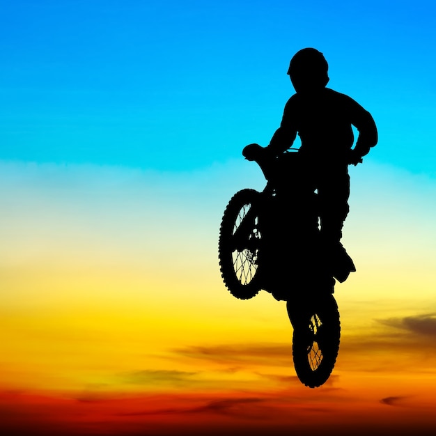 silhueta de piloto de motocross saltar no céu ao pôr do sol