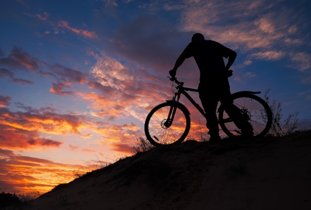 Silhueta de praticante de esportes, andar de bicicleta no Prado, o belo pôr do sol. Jovem andando de bicicleta.