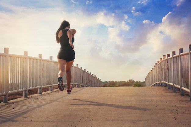 silhueta de treino de corrida de mulher em forma do outro lado da ponte enquanto maratona praticando ao pôr do sol