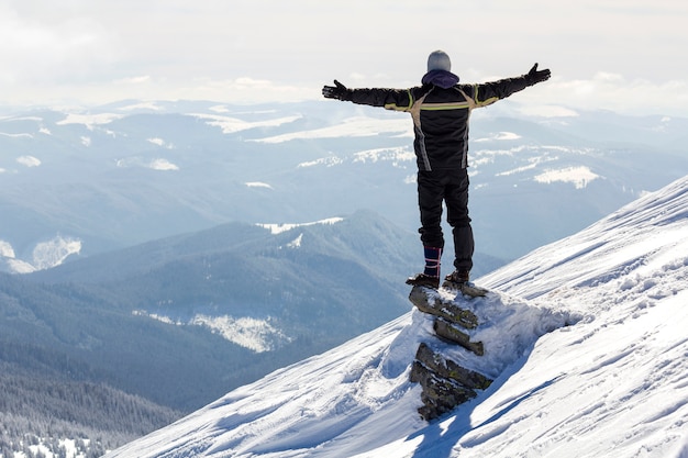 Silhueta de turista sozinho em pé no topo da montanha de neve em pose de vencedor com as mãos levantadas, apreciando a vista e realização em dia ensolarado brilhante de inverno. Aventura, atividades ao ar livre, estilo de vida saudável.