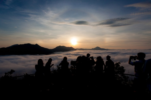 Silhueta de turistas olhando a névoa e a montanha com fundo de natureza do nascer do sol