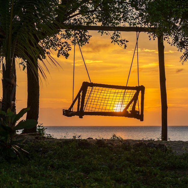 Silhueta de um balanço de madeira com um belo pôr do sol na praia tropical perto do mar, ilha de zanzibar, tanzânia, áfrica oriental