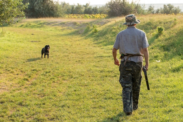 Silhueta de um caçador com uma arma nos juncos contra o sol, uma emboscada para patos com cães