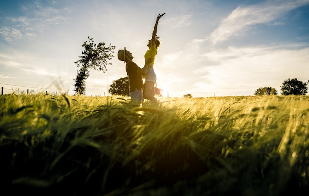 Silhueta de um casal apaixonado, pulando com os braços erguidos em um campo de trigo ao pôr do sol.