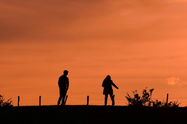 Silhueta de um casal caminhando na montanha com um pôr do sol