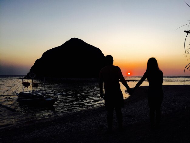 Silhueta de um casal de mãos dadas contra o mar durante o pôr-do-sol