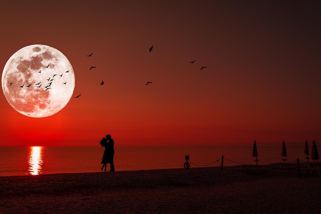 Silhueta de um casal se beijando sob a lua cheia ao pôr do sol