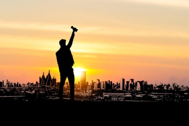 Silhueta de um empresário de sucesso levanta o troféu com o fundo do pôr do sol do céu noturno da cidade, celebrando o homem segurando o troféu da taça vencedora