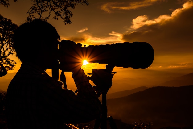 Silhueta de um fotógrafo de paisagem usar super teleobjectiva no topo de montanhas durante o céu pôr do sol
