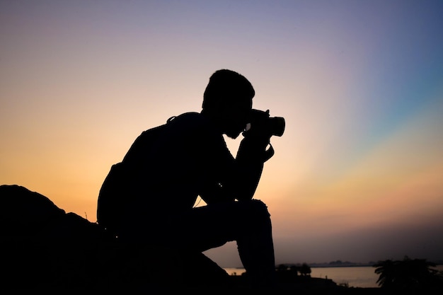 Silhueta de um fotógrafo durante o pôr do sol segurando a câmera na mão Copie o espaço