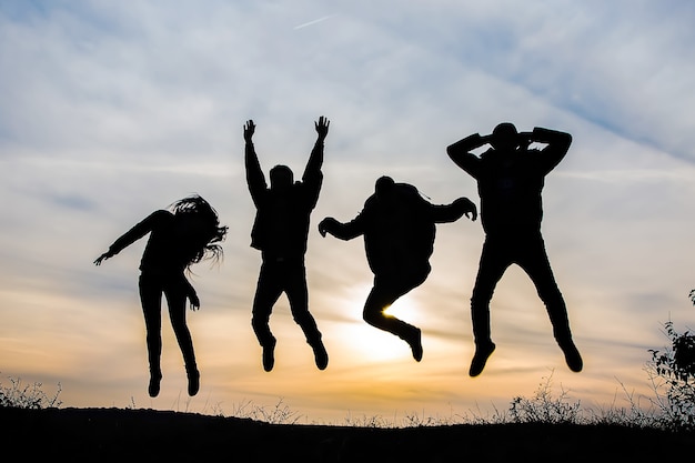 Foto silhueta de um grupo de quatro pessoas felizes pulando ao pôr do sol