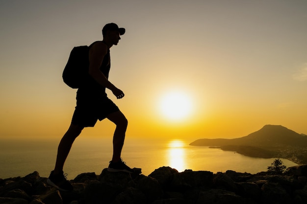 Silhueta de um homem andando nas rochas das montanhas enquanto caminhava ao pôr do sol