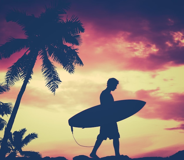 Silhueta de um homem caminhando segurando uma prancha de surf contra o céu laranja