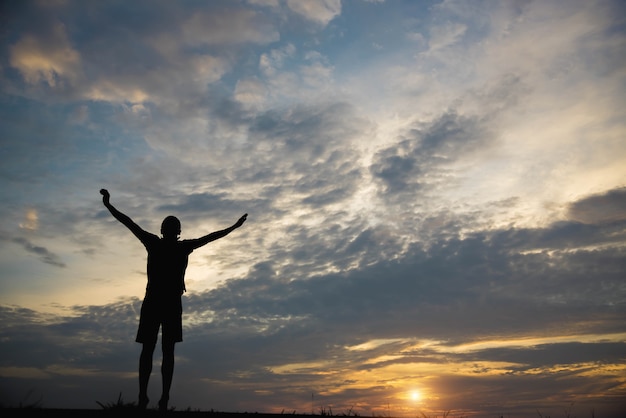 Silhueta de um homem com as mãos levantadas por do sol.