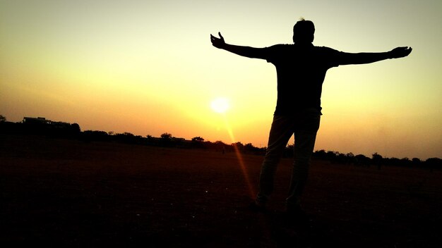 Silhueta de um homem com os braços estendidos de pé no campo ao pôr do sol