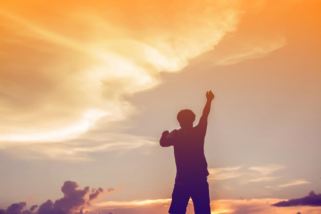 Foto silhueta de um homem com os braços levantados de pé contra o céu durante o pôr do sol