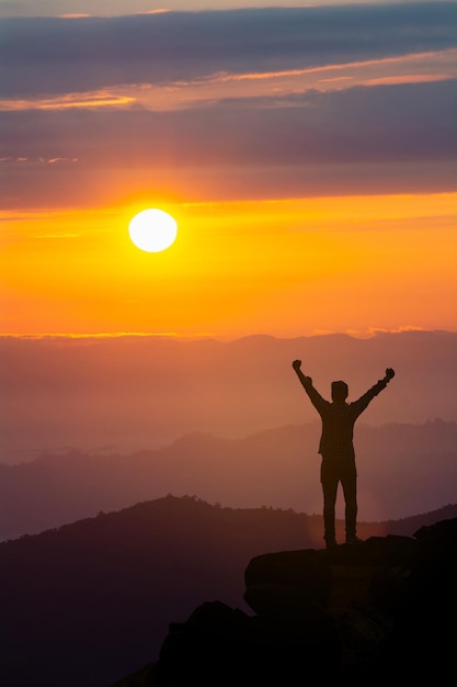 Foto silhueta de um homem com os braços levantados de pé na montanha contra o céu durante o pôr do sol