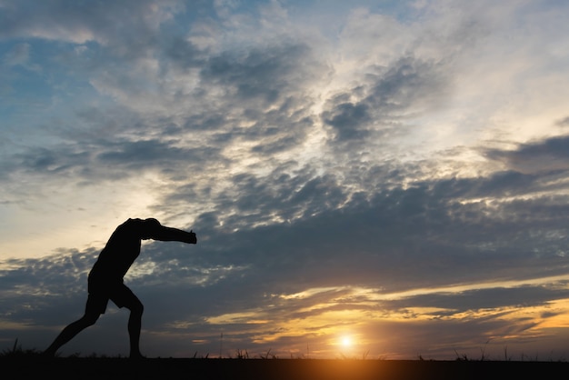 Silhueta de um homem com um homem exercitando-se por do sol.