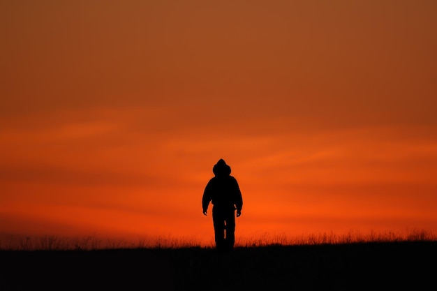 Silhueta de um homem de capuz indo para o pôr do sol. Silhueta ao pôr do sol vermelho-alaranjado.