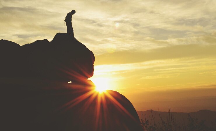 Foto silhueta de um homem de pé no penhasco contra o sol brilhante