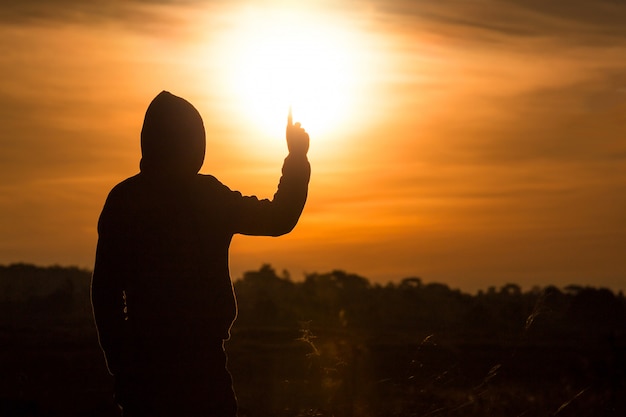 Foto silhueta de um homem em pé e levante as mãos no ar durante o pôr do sol