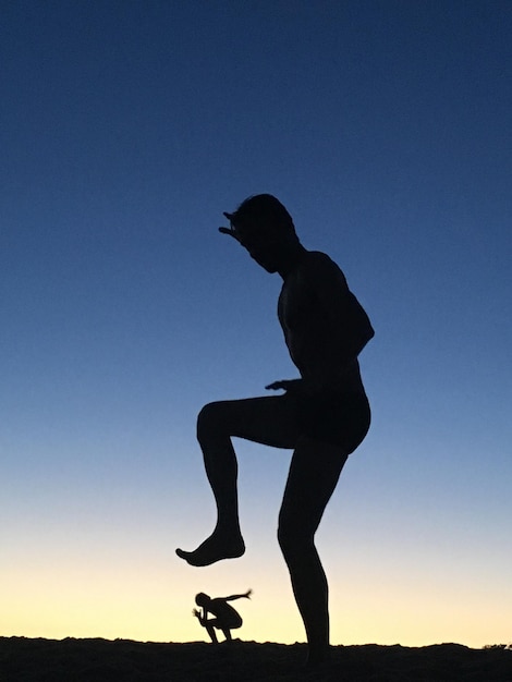 Foto silhueta de um homem jogando uma pessoa contra o céu ao anoitecer