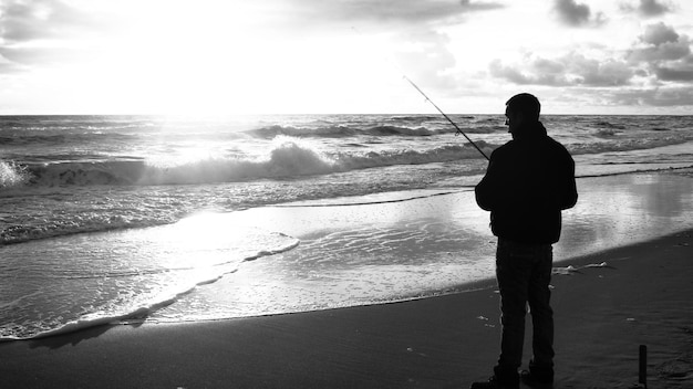 Foto silhueta de um homem pescando na costa durante o pôr do sol