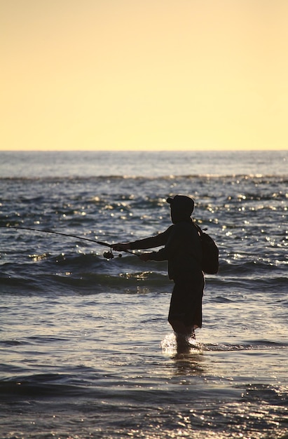 Foto silhueta de um homem pescando no mar ao pôr-do-sol