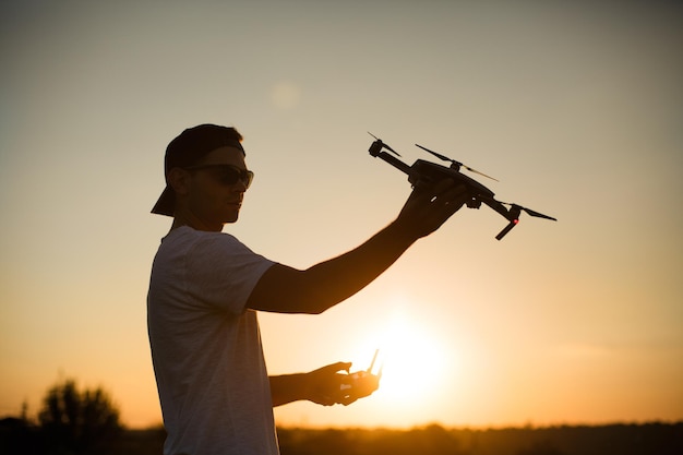 Silhueta de um homem segurando um pequeno drone compacto e controle remoto em suas mãos lança piloto