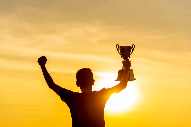 Silhueta de um homem vencedor segurando o prêmio da taça do troféu de ouro.