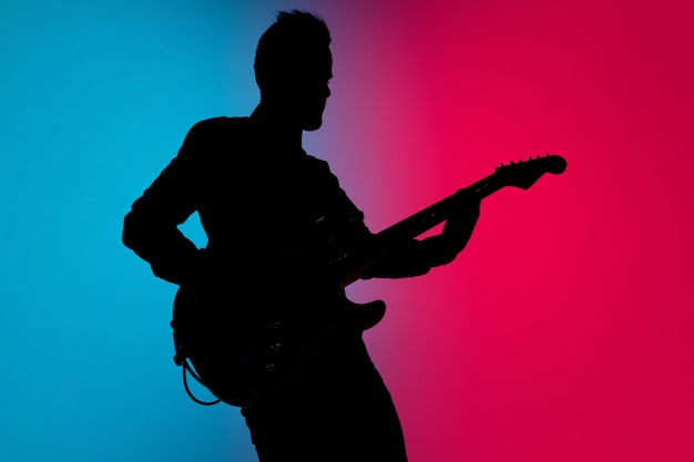 Foto silhueta de um jovem guitarrista caucasiano isolado em um estúdio gradiente rosa-azulado em luz de néon