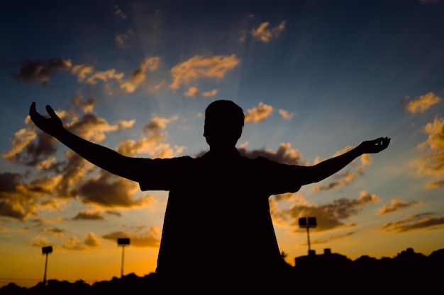 Foto silhueta de um jovem livre com os braços abertos ao pôr do sol.