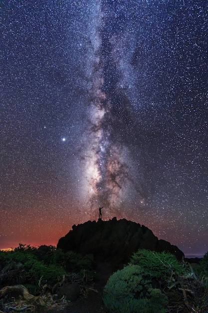 Silhueta de um jovem sob as estrelas olhando para a Via Láctea à noite, astrofotografia