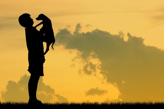 Foto silhueta de um menino com um cão no campo contra o céu durante o pôr do sol