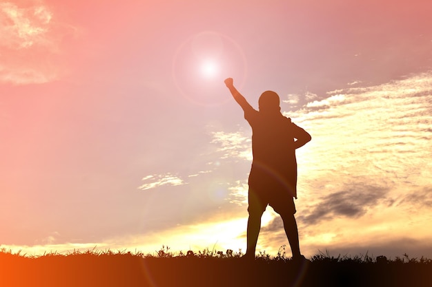 Foto silhueta de um menino de pé com o braço levantado contra o céu durante o pôr do sol